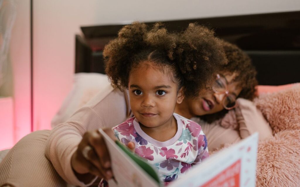 A mother and daughter sharing a heartfelt moment reading a book in bed.