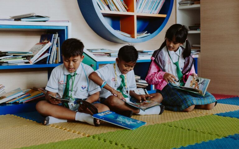 Three children in school uniforms reading books together in a vibrant library setting.