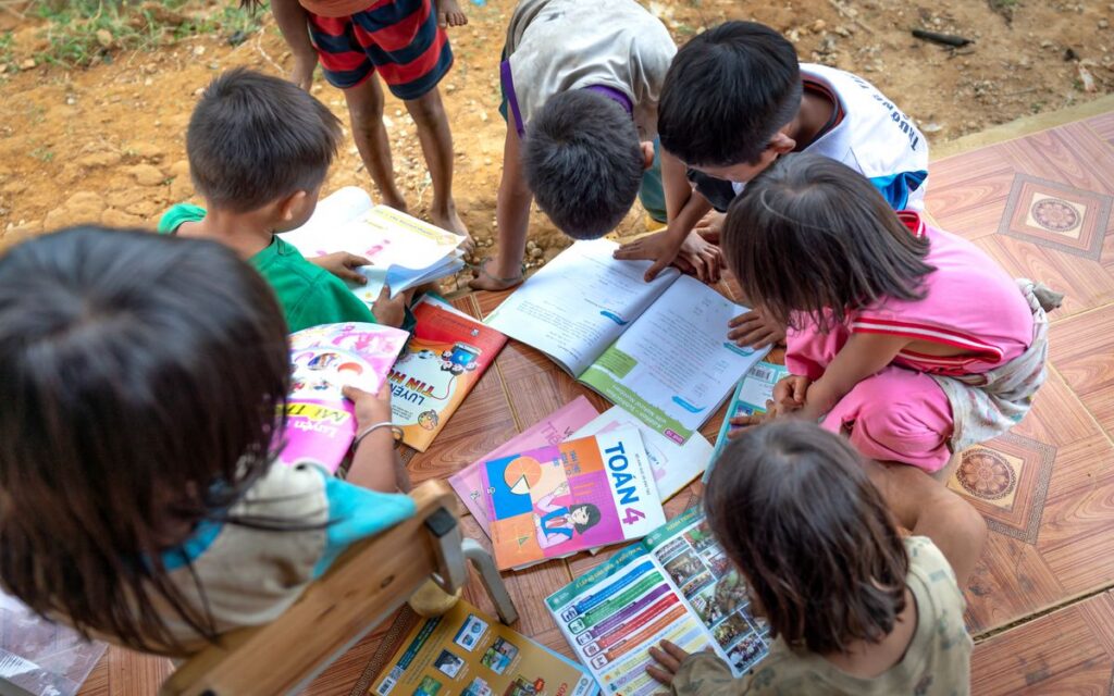 Children gathered outdoors, actively engaged in reading and learning from books.