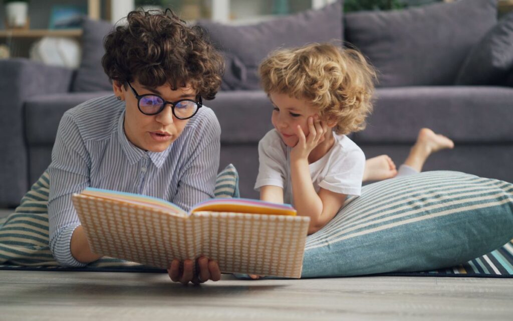 Woman reading a book to her son while lying on the floor at home.
