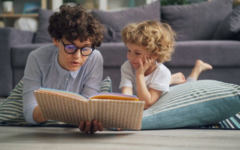 Woman reading a book to her son while lying on the floor at home.