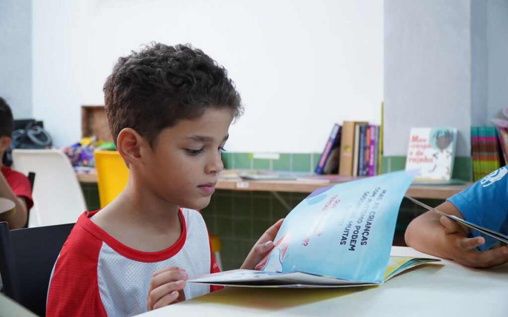 A young boy engrossed in reading a book in a classroom environment, promoting child literacy.