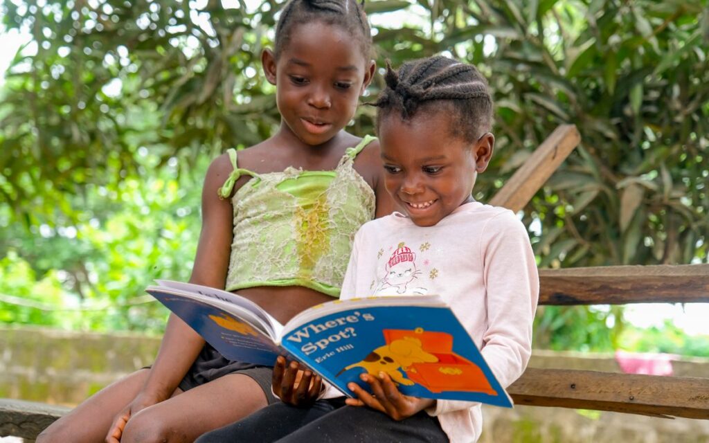 Two children enjoying a storybook outdoors, sharing a joyful reading moment.