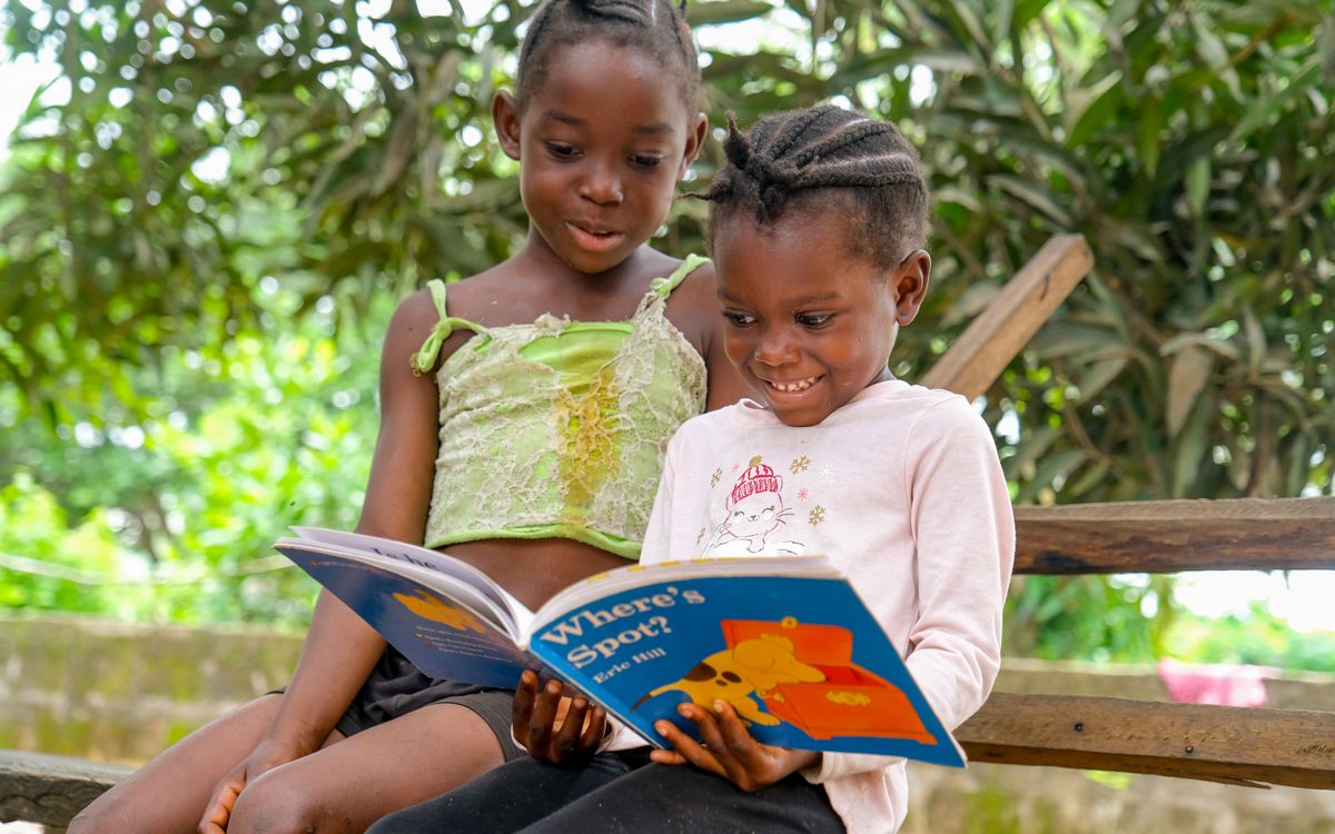 Two children enjoying a storybook outdoors, sharing a joyful reading moment.