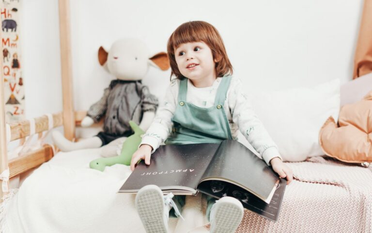 Adorable child sitting on a bed, enjoying a book in a bright playroom with toys.