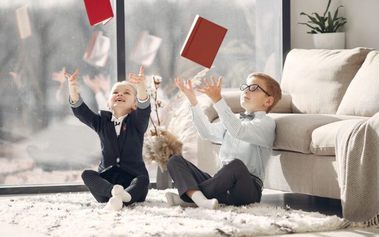 Cute children coworkers in uniform and eyeglasses throwing up organizers and laughing after working day in cozy atmosphe