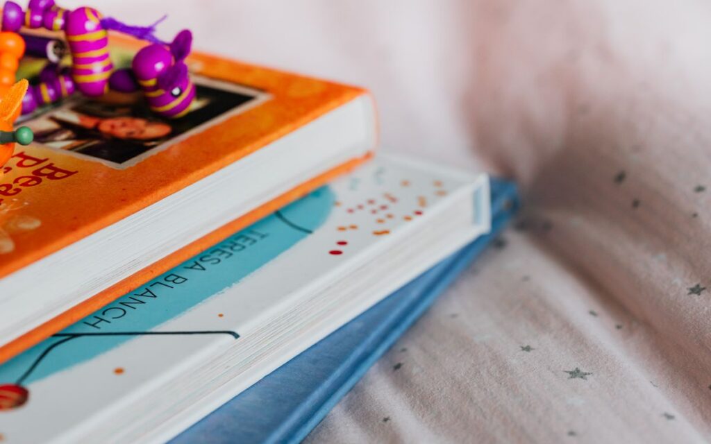 Close-up of colorful children's books stacked with a playful toy on top indoors.