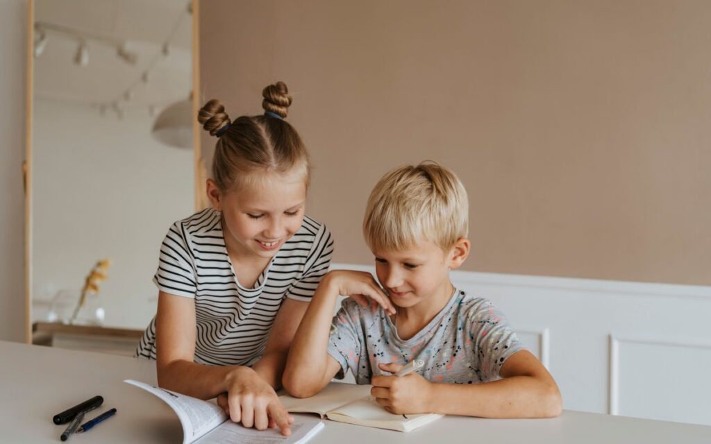Two kids studying together at home, focusing on a book in a calm, indoor setting.