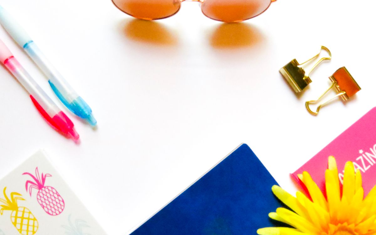Bright flat lay of stationery with sunglasses and a decorative flower on white background.
