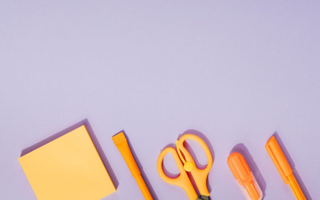 Bright orange office supplies neatly arranged on a pastel purple background, ideal for creative design projects.