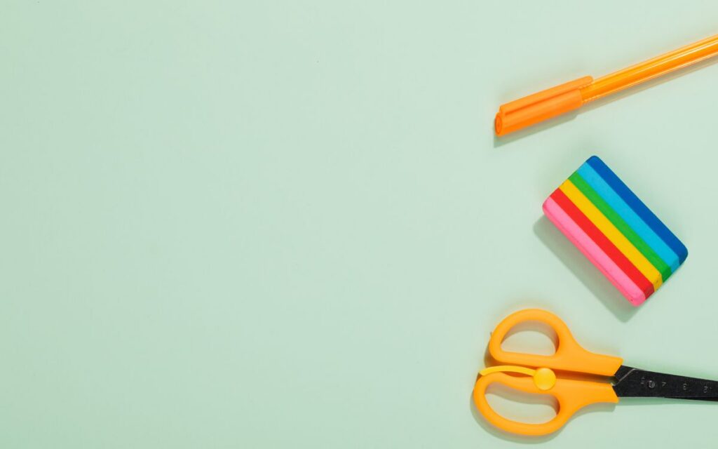 Flat lay of colorful office supplies including pen, eraser, and scissors on a pastel green background.