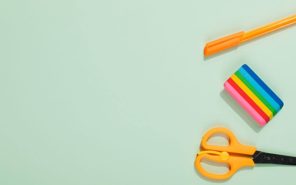 Flat lay of colorful office supplies including pen, eraser, and scissors on a pastel green background.