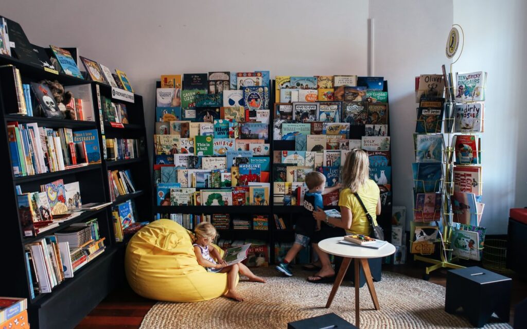 A mother and children enjoy reading in a colorful library section with diverse book selections.