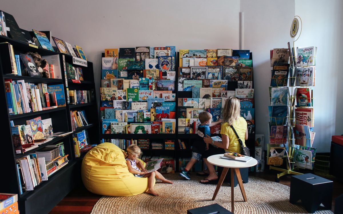 A mother and children enjoy reading in a colorful library section with diverse book selections.