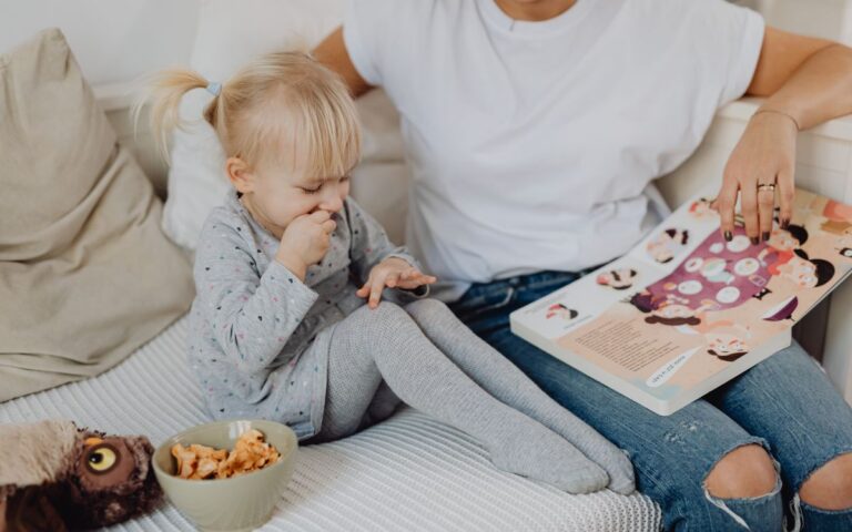 A mother and daughter enjoying storytime on a cozy couch with snacks nearby.