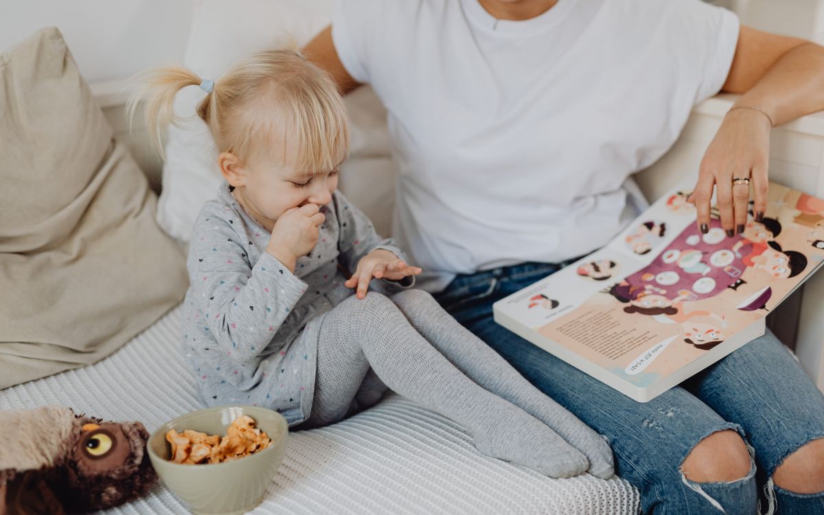 A mother and daughter enjoying storytime on a cozy couch with snacks nearby.