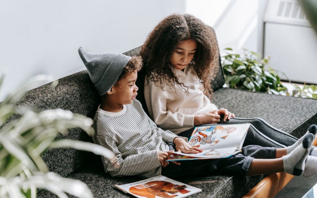 From above of concentrated African American boy and girl discussing pictures in book on couch