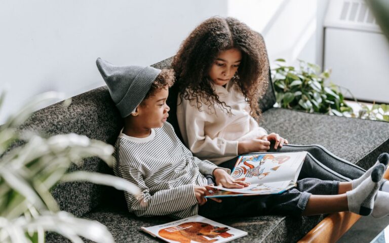 From above of concentrated African American boy and girl discussing pictures in book on couch
