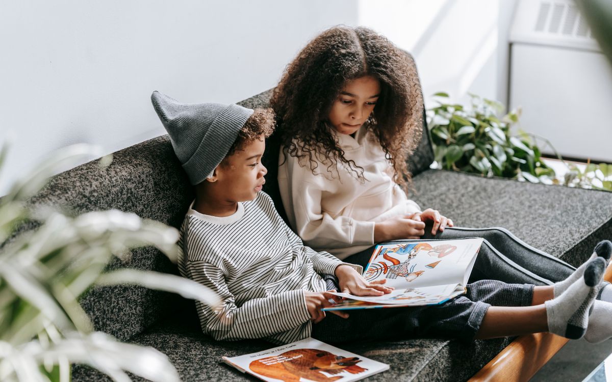 From above of concentrated African American boy and girl discussing pictures in book on couch