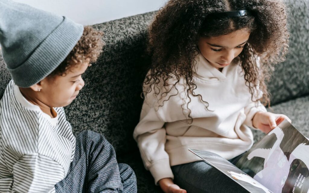From above of crop African American boy and girl watching pictures of animals in magazine