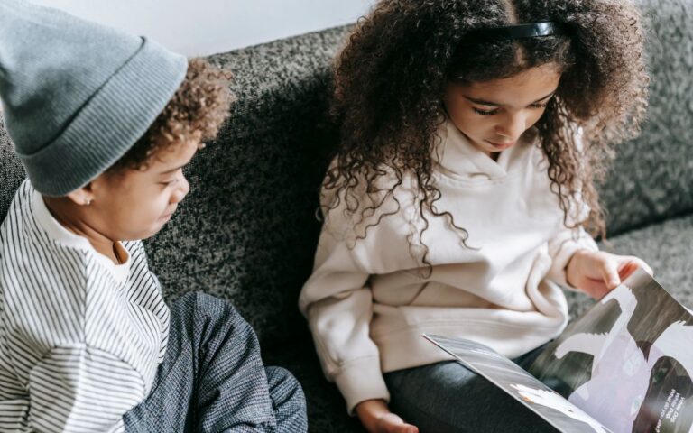 From above of crop African American boy and girl watching pictures of animals in magazine