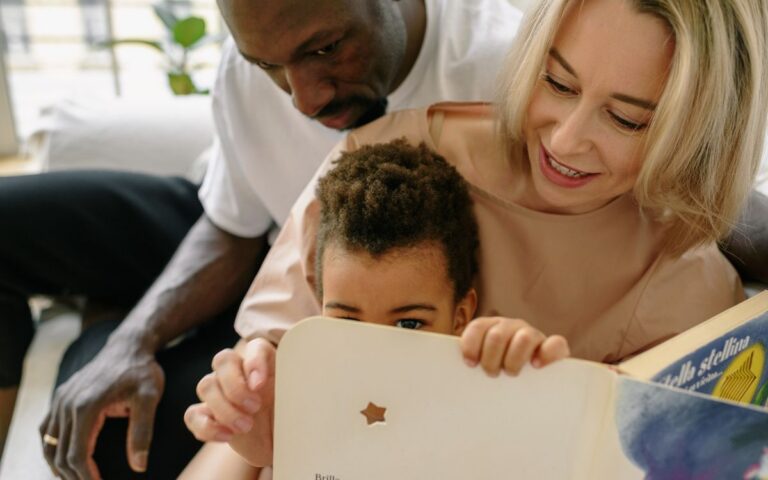 Interracial family enjoying quality time reading a book indoors together.