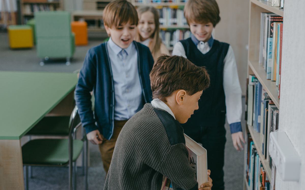 Group of children interacting by bookshelves in a school library environment.