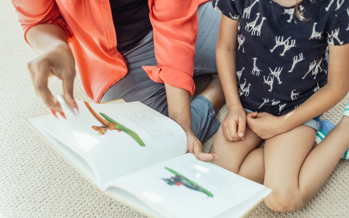 A mother and daughter sit on the floor, engaged in reading a colorful children's book.