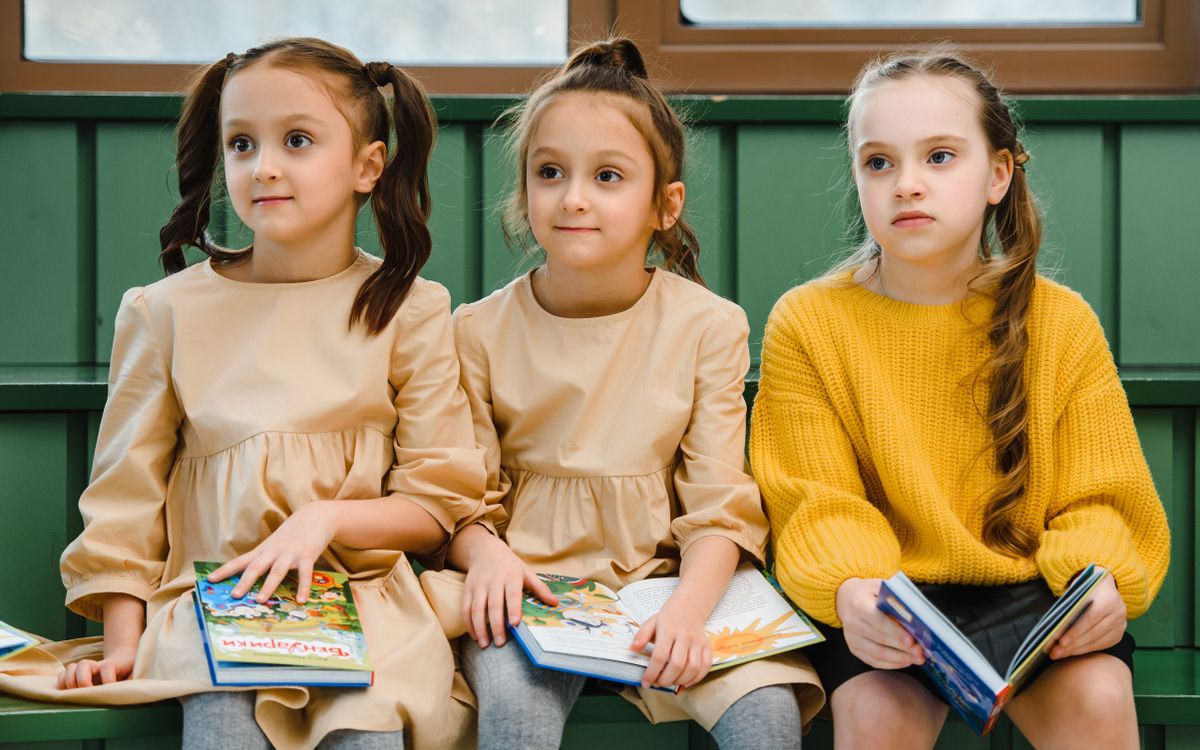 Three young girls reading books indoors, showcasing education and learning in a warm setting.