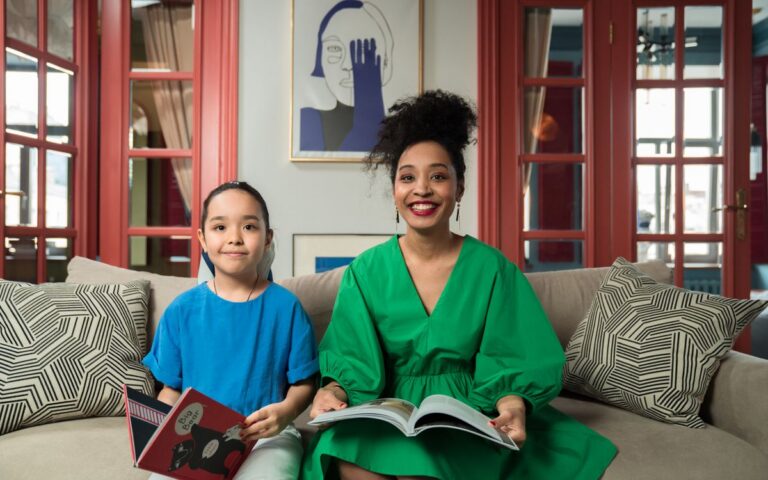 A smiling mother and daughter reading books together on a comfortable sofa in a bright, inviting room.