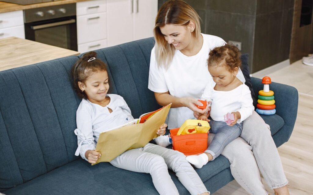 A mother reading with her daughters on a sofa, enjoying family time indoors.