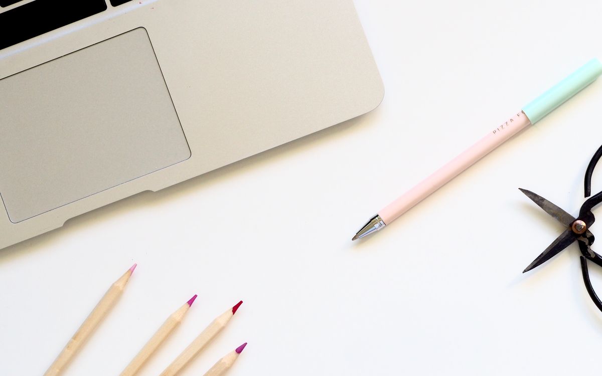 A clean minimalist desk setup featuring a laptop and colorful stationery in a home office.