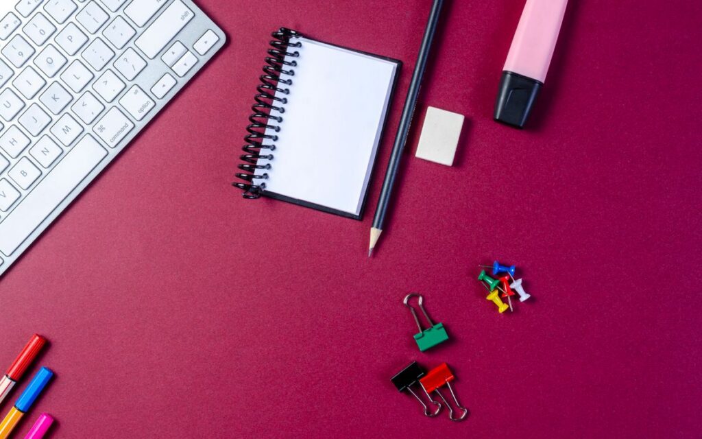 Flat lay of stationery items and keyboard on a vibrant desk.