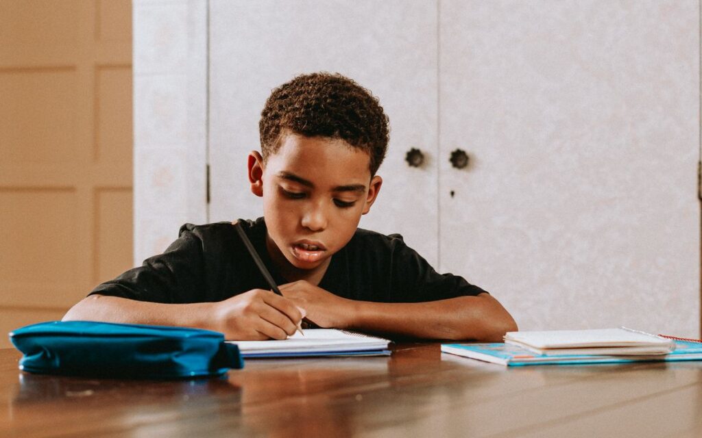 Young boy concentrating on writing at a desk, symbolizing education and learning.