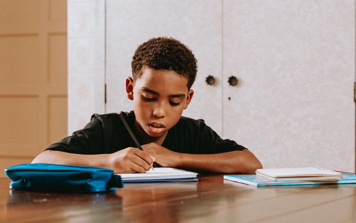 Young boy concentrating on writing at a desk, symbolizing education and learning.