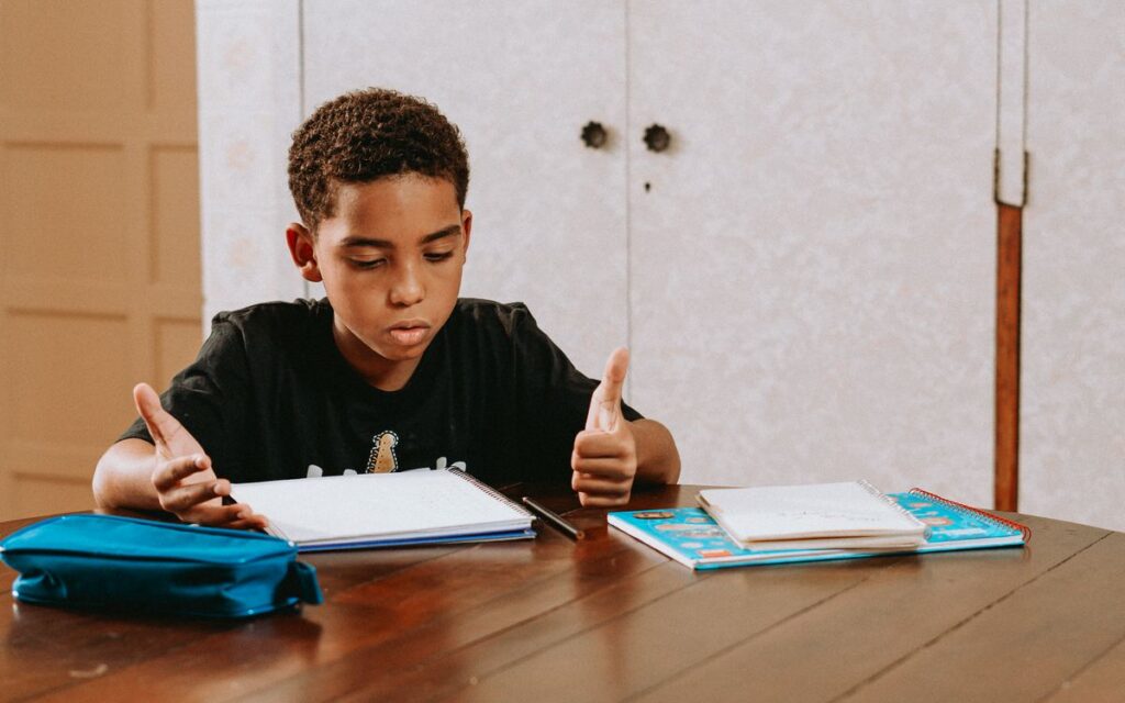 A boy engrossed in his homework, seated at a wooden table with notebooks and a pencil case.