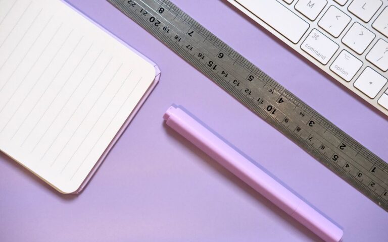 Flat lay of a pastel-colored workspace featuring a notebook, ruler, highlighter, and keyboard.