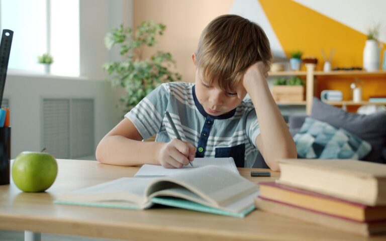 Young boy concentrating on homework at desk in a colorful room.