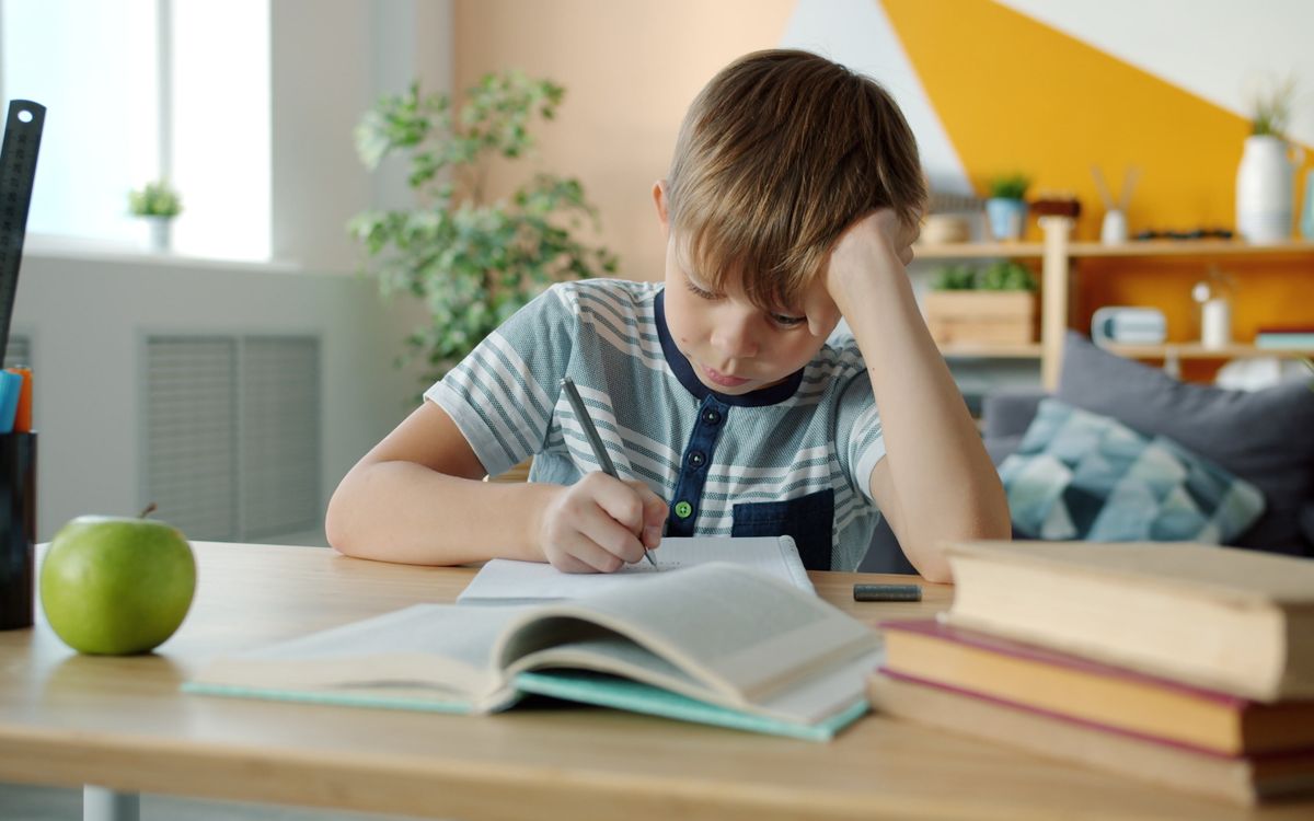Young boy concentrating on homework at desk in a colorful room.