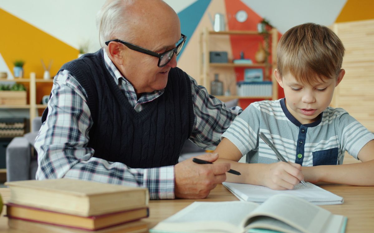 Senior man assisting young boy with schoolwork indoors, fostering learning.