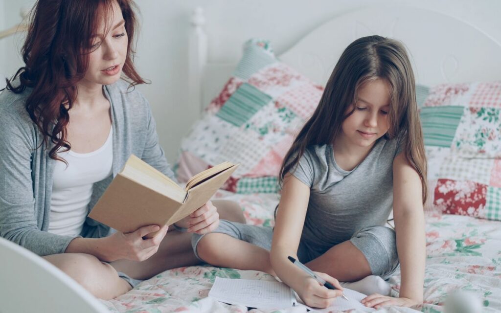 Mother and daughter bonding through reading and writing on a cozy bed.