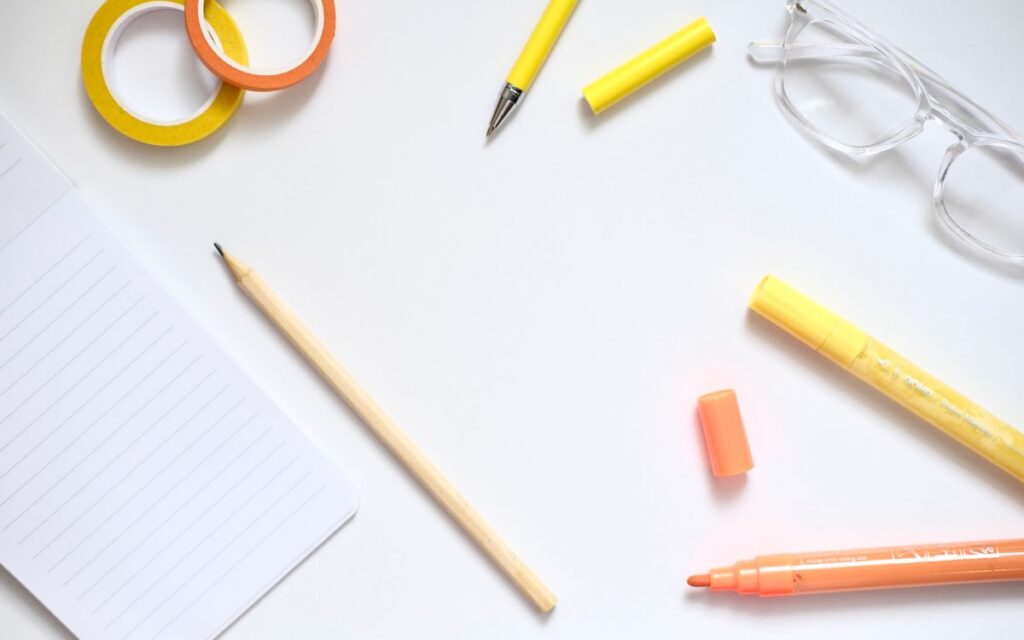 Flat lay of stationery items on a desk with a minimalist aesthetic and bright colors.