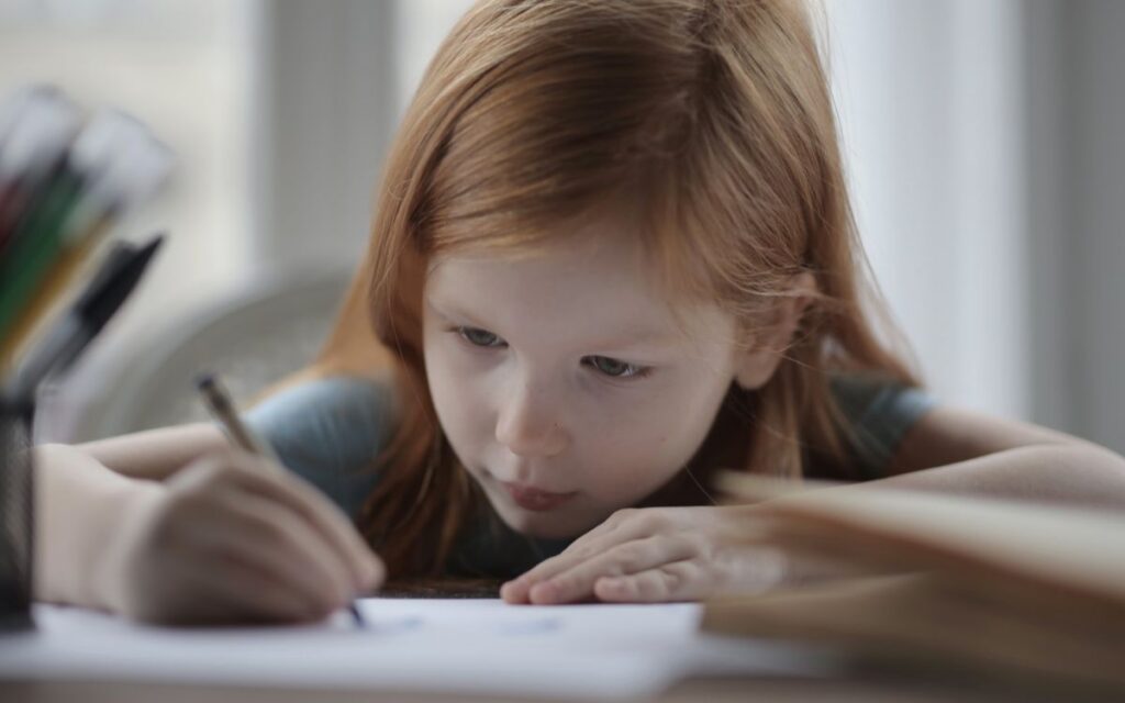 A young girl intently writing while doing homework indoors, symbolizing concentration and learning.