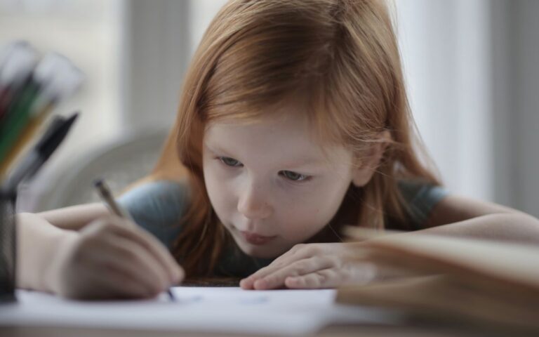 A young girl intently writing while doing homework indoors, symbolizing concentration and learning.