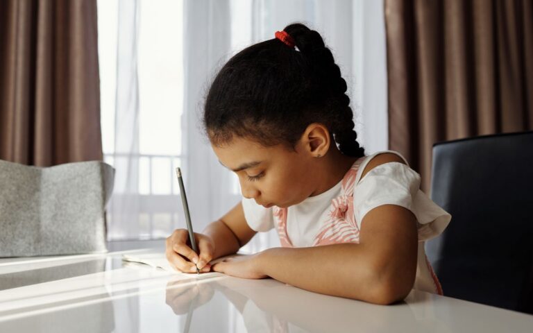 A focused young girl writing at her desk, absorbed in her homework task at home.