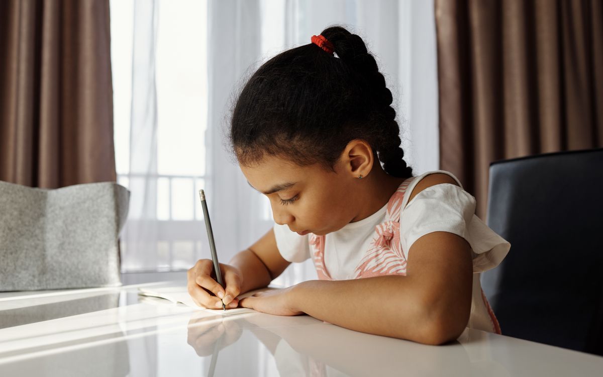 A focused young girl writing at her desk, absorbed in her homework task at home.