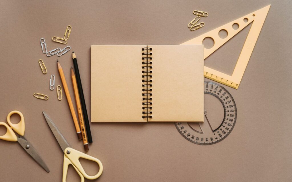Flat lay of school supplies featuring a spiral notebook, scissors, and stationery on a brown background.