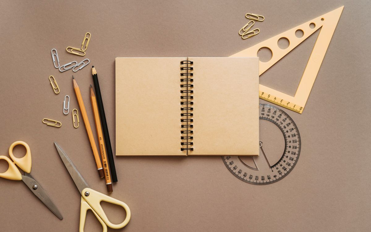 Flat lay of school supplies featuring a spiral notebook, scissors, and stationery on a brown background.