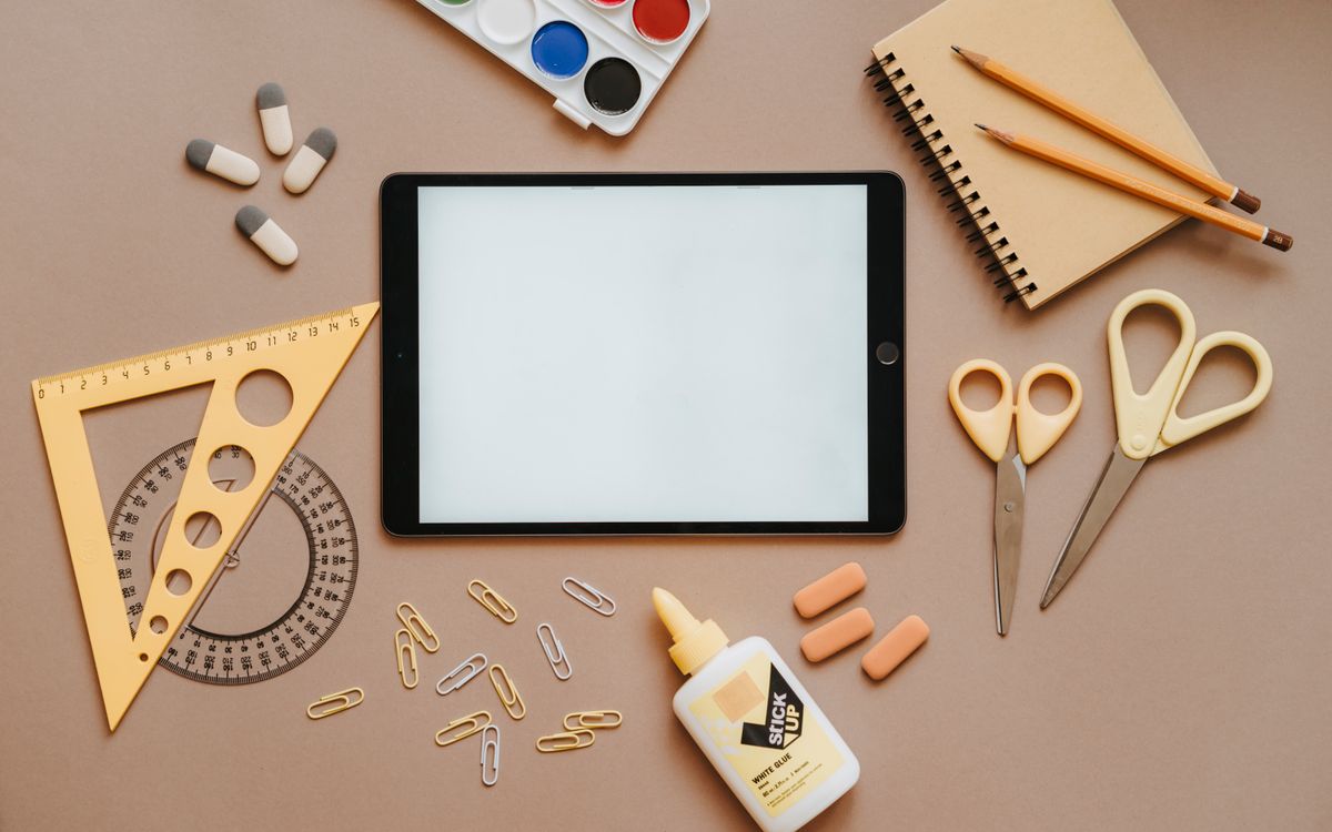 Flat lay of school supplies including tablet, scissors, glue, and stationery. Ideal for education themes.