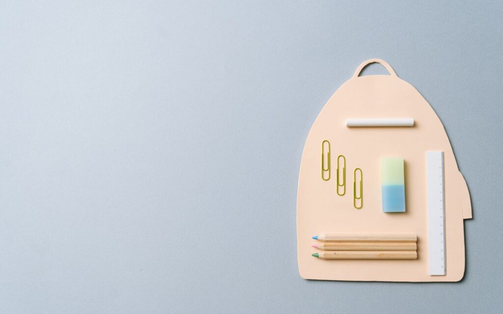 Minimalist top view of school supplies creatively arranged on a backpack-shaped platform.